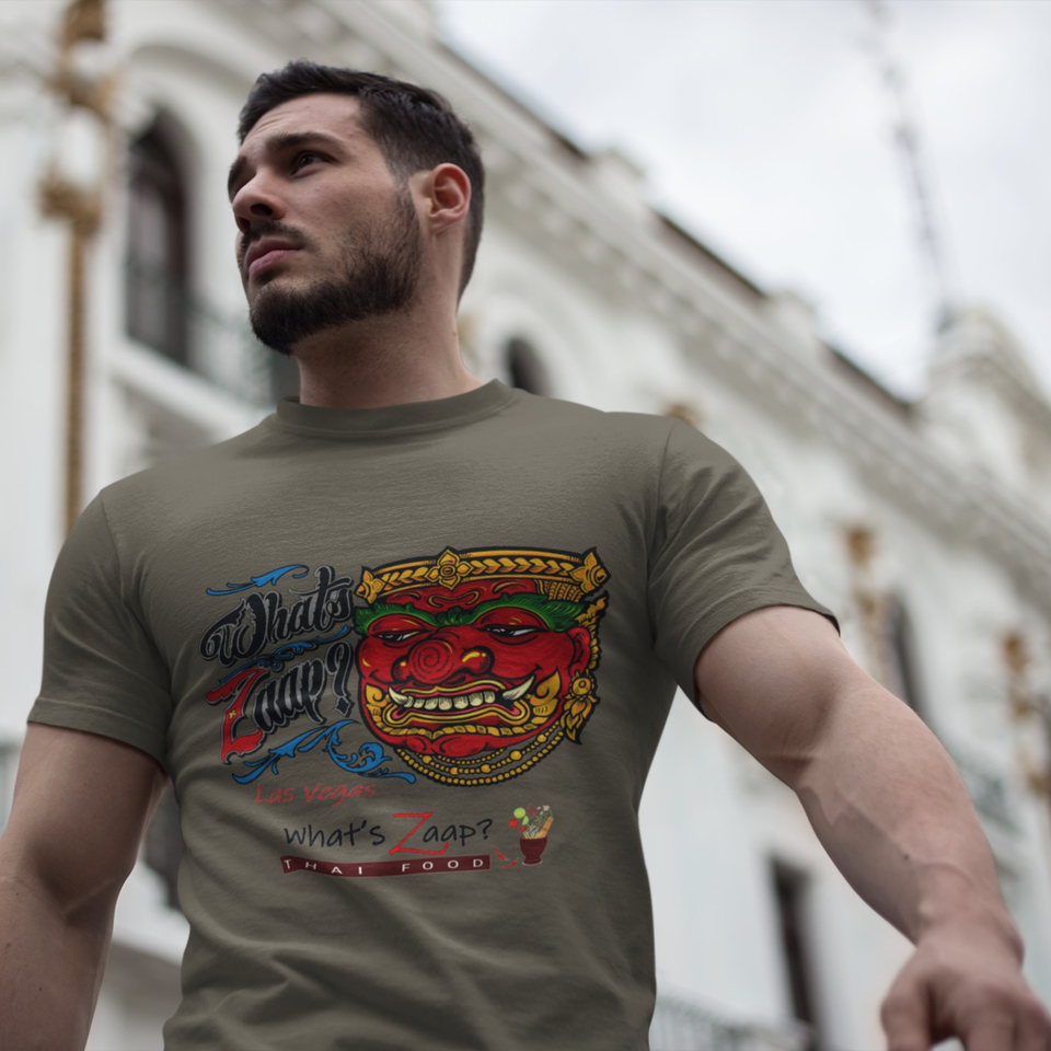 Bearded man wearing a graphic What Zap Thai Food Las Vegas T-shirt, standing outdoors against blurred ornate buildings.