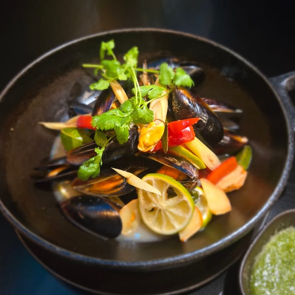 Steamed mussels in a black bowl, garnished with lime, chili, lemongrass, and cilantro.