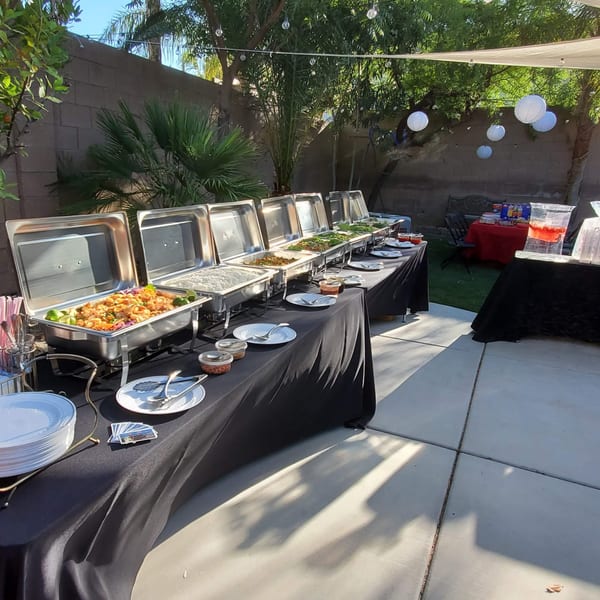 An outdoor Thai food buffet with multiple chafing dishes filled with various dishes and drinks.