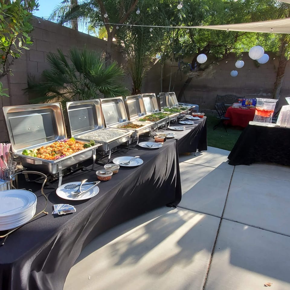 An outdoor Thai food buffet with multiple chafing dishes filled with various dishes and drinks.