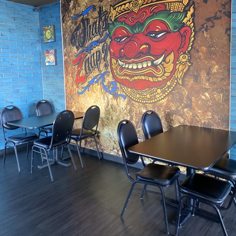 Interior of What's Zaap? Thai Food, with black tables and chairs, and a large Thai mural.