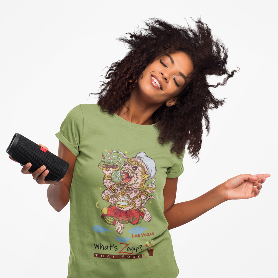 Smiling woman with curly hair holds a portable speaker, wearing a green What's Zaap Thai Food Las Vegas T-shirt against a white background.