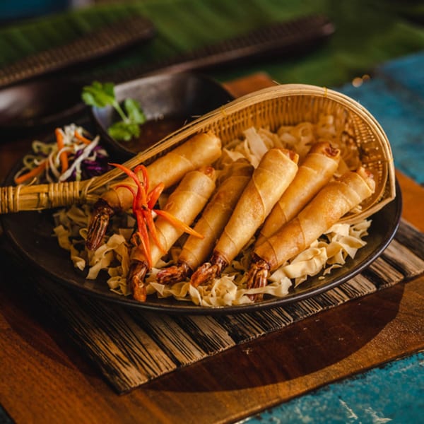 Crispy fried shrimp spring rolls with chili garnish, served on a bed of noodles with dipping sauce.