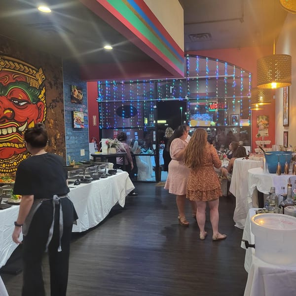 A vibrant Thai restaurant interior with a large red mural, buffet tables, and guests mingling.