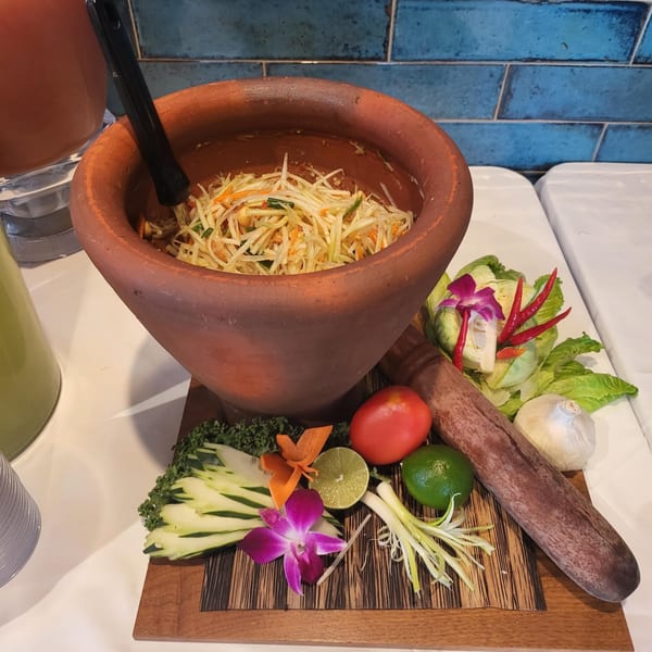 Thai papaya salad in a large mortar with fresh ingredients like lime, tomato, and chili.