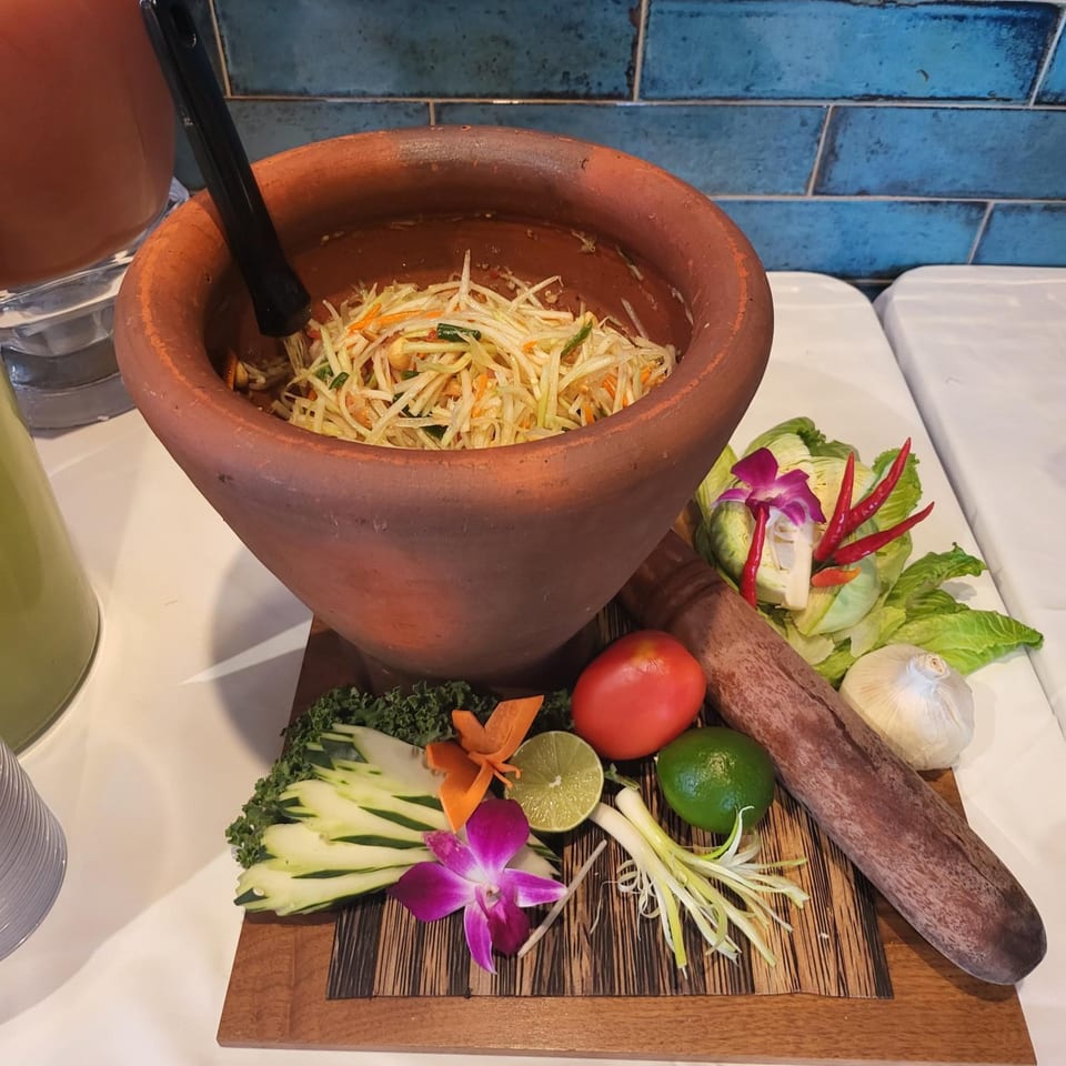 Thai papaya salad in a large mortar with fresh ingredients like lime, tomato, and chili.
