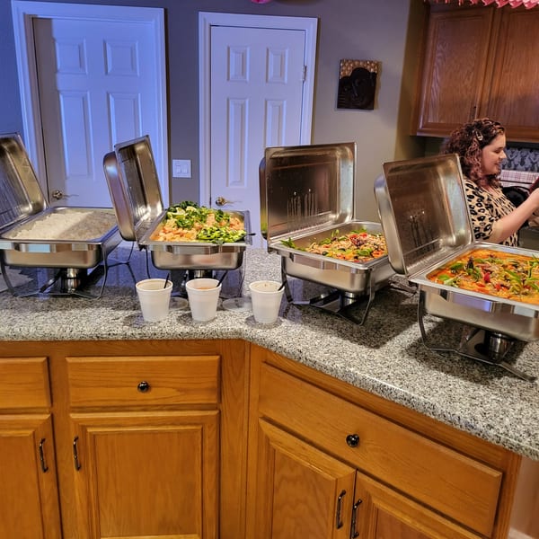 Four chafing dishes filled with various Thai dishes, including rice, on a kitchen counter.