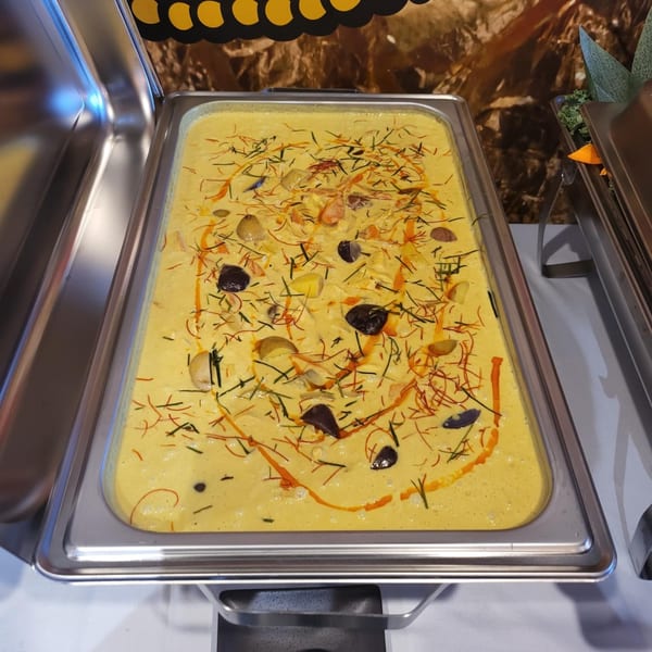 A large buffet tray of yellow Thai curry with herbs, spices, and vegetables.