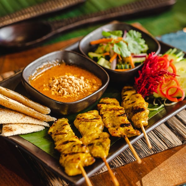 Thai chicken satay skewers with peanut sauce, toast, and a side salad on a dark plate.
