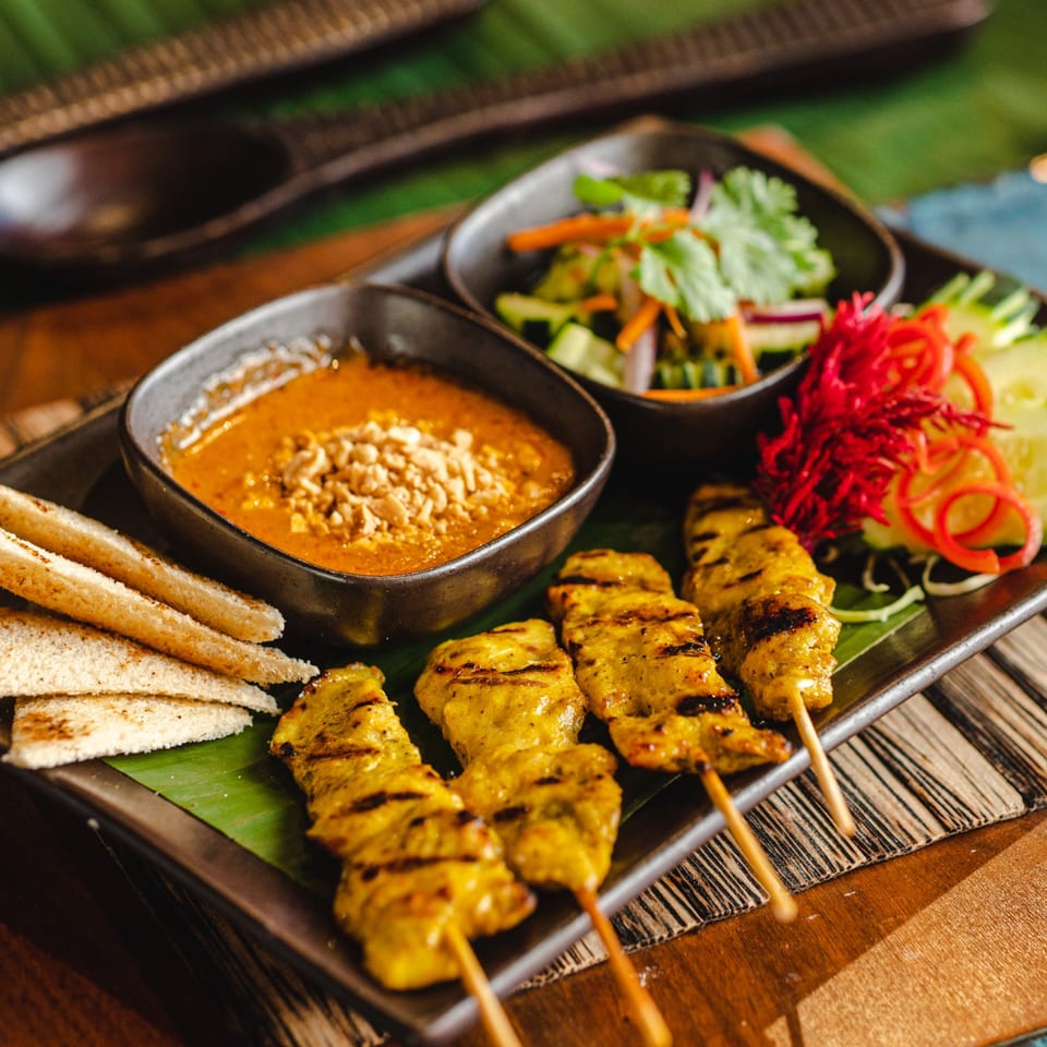 Thai chicken satay skewers with peanut sauce, toast, and a side salad on a dark plate.