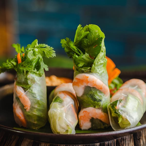 Fresh Thai spring rolls with shrimp, lettuce, and cilantro on a dark plate.