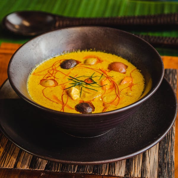 A dark bowl of yellow Thai curry with mushrooms and herbs, on a wooden coaster.