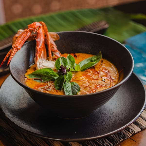 Thai red curry with crab and basil in a black bowl on a banana leaf.