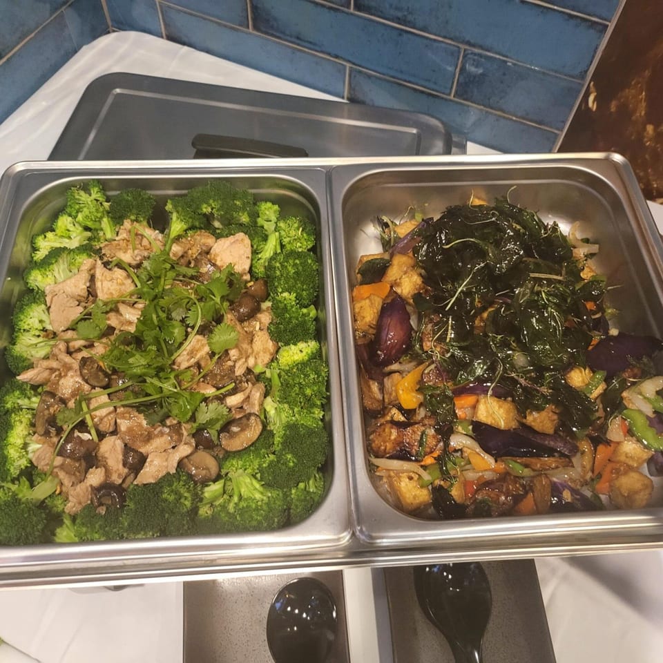 Two buffet trays of Thai food: one with chicken, mushrooms, and broccoli, the other with eggplant and tofu.