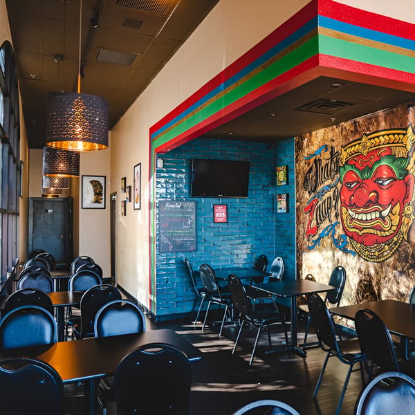 Interior of What's Zaap? Thai Food, featuring colorful decor, black tables, and a large mural.