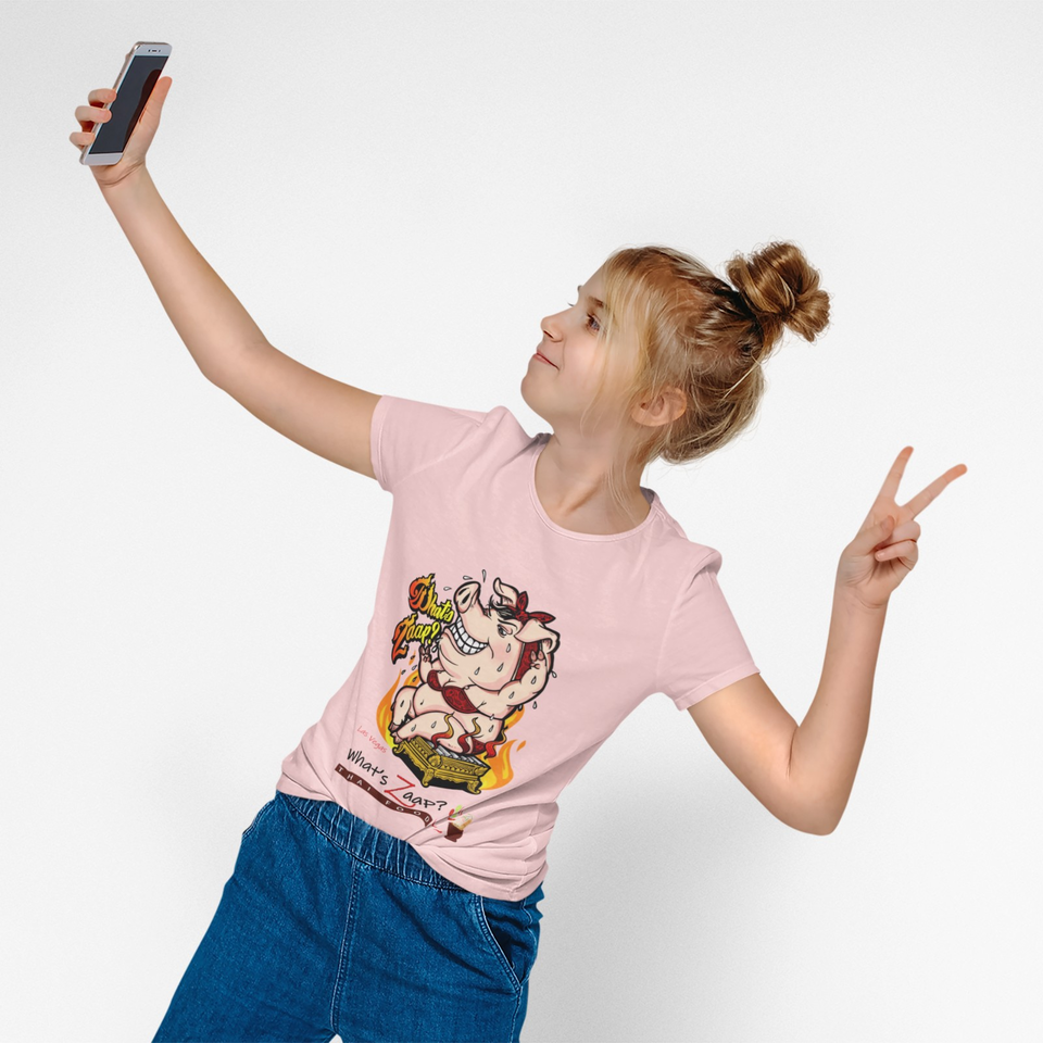 Young woman takes a selfie while making a peace sign, wearing a pink cartoon graphic shirt against a white background.
