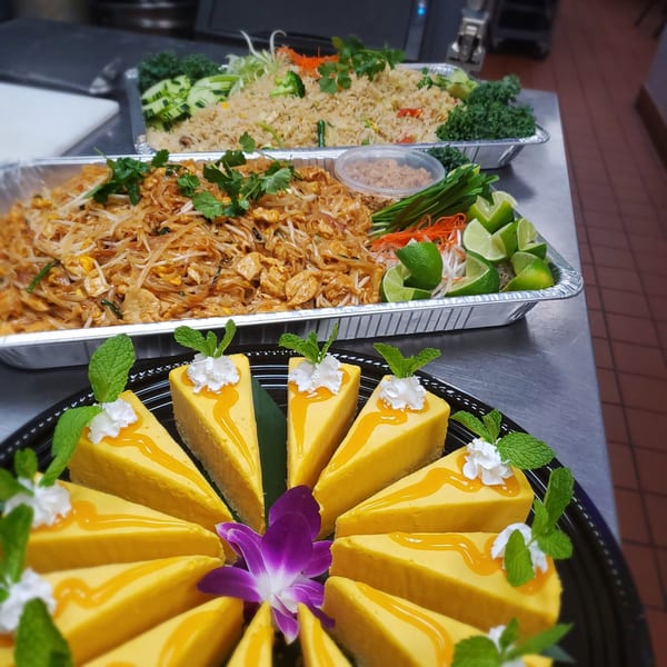 Thai catering spread with Pad Thai, fried rice, and mango cheesecake slices with mint and whipped cream.