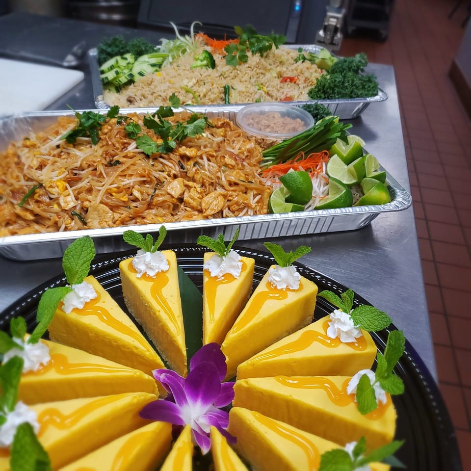 Thai catering spread with Pad Thai, fried rice, and mango cheesecake slices with mint and whipped cream.