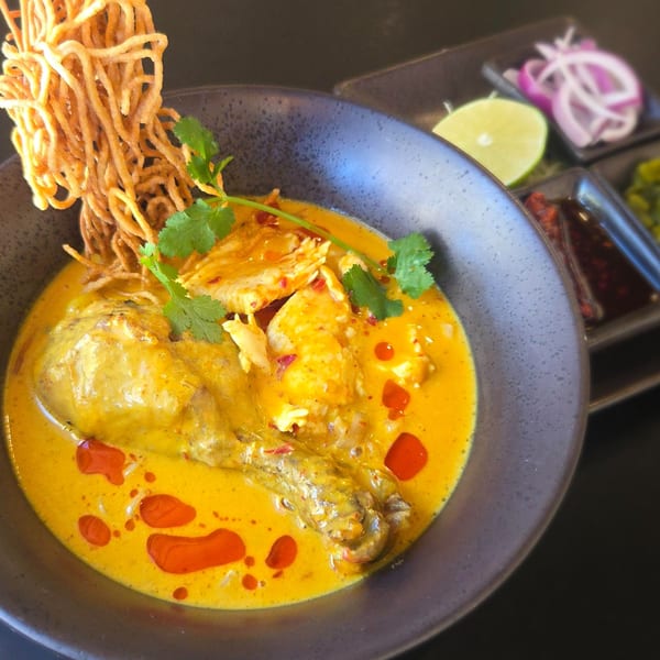 Zaap's Thai Khao Soi with chicken, crispy noodles, cilantro, and chili oil, with sides of lime and onions.