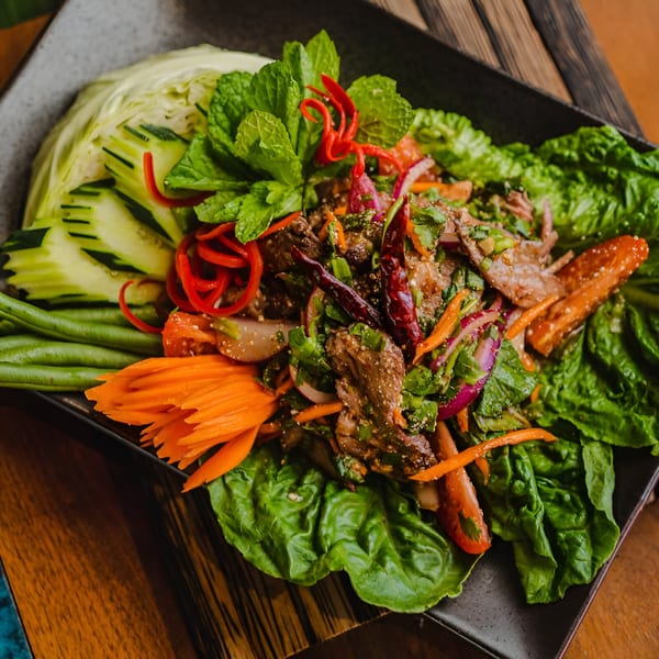 Thai beef salad with fresh mint, red chilies, and vegetables on a dark plate.